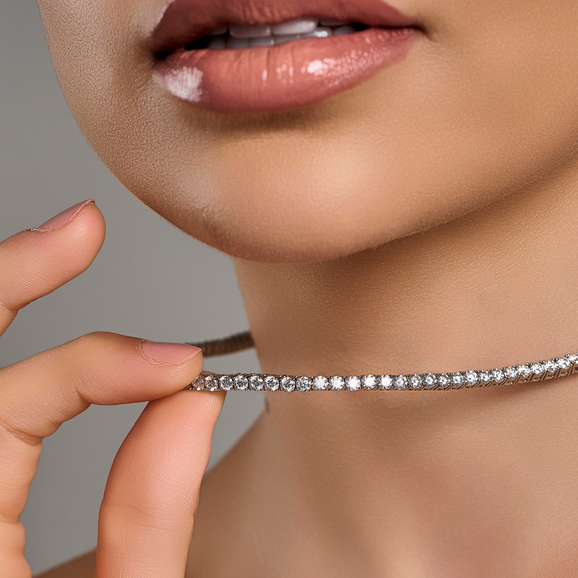 Lifestyle close-up of a woman holding a luxury tennis necklace with brilliant cut moissanite stones in 925 sterling silver.