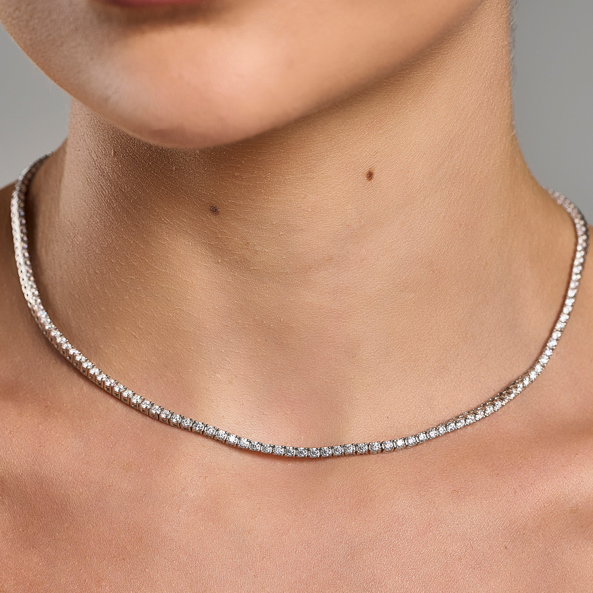 Lifestyle close-up of a woman holding a luxury tennis necklace with brilliant cut moissanite stones in 925 sterling silver.