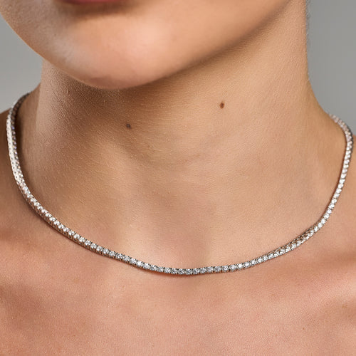 Lifestyle close-up of a woman holding a luxury tennis necklace with brilliant cut moissanite stones in 925 sterling silver.