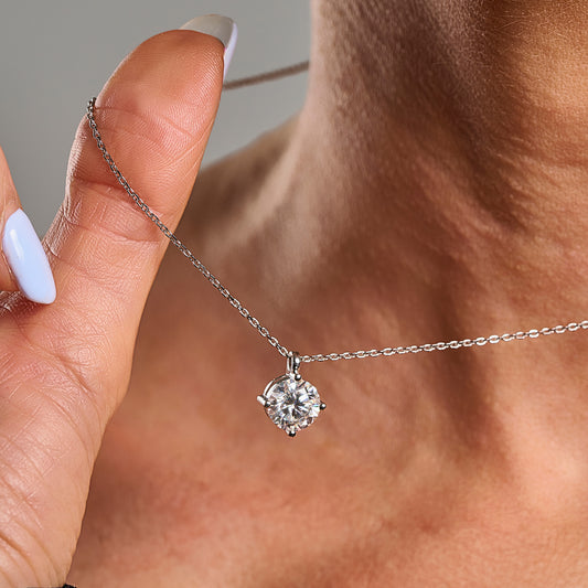Lifestyle close-up of a Light Point necklace with 2 ct round brilliant cut moissanite in 925 sterling silver held delicately by hand.
