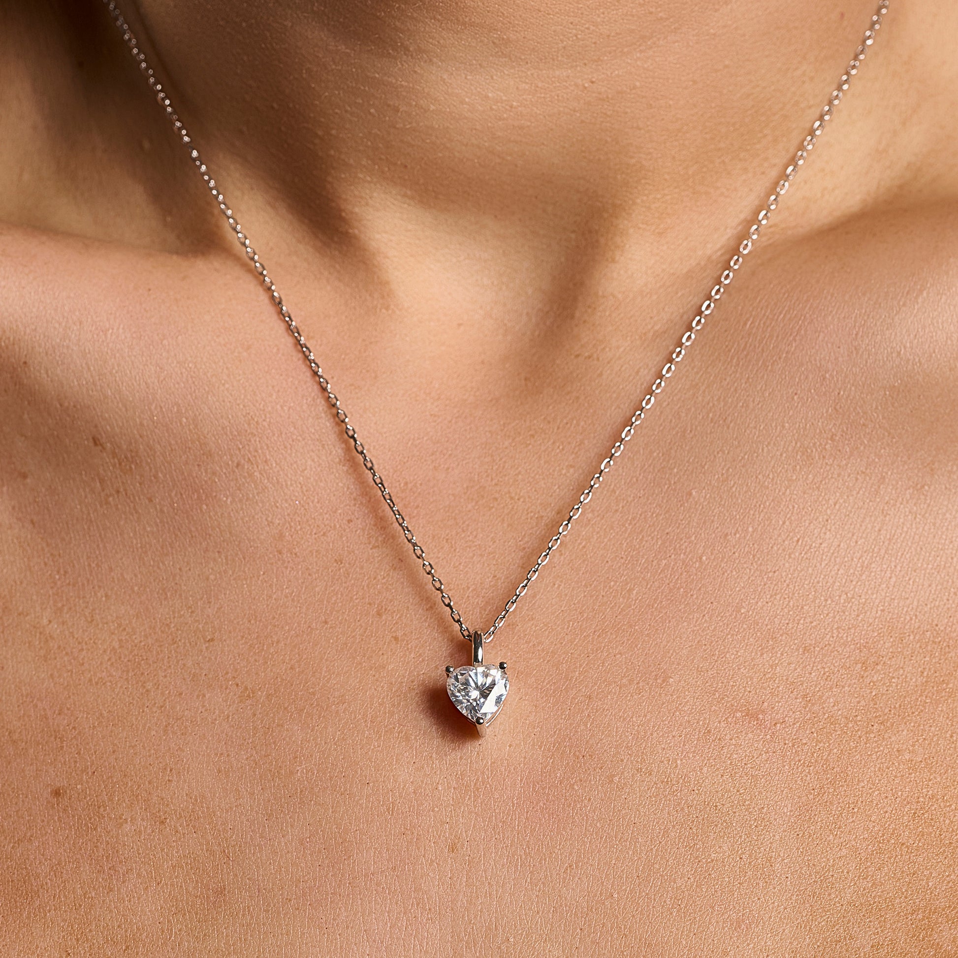 Model wearing a 925 sterling silver necklace with a 2 ct heart cut moissanite pendant in a minimalist neckline close-up.