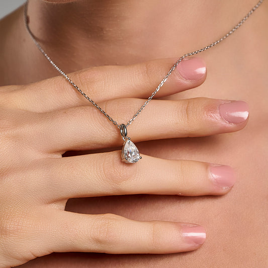Model wearing a 925 sterling silver necklace with a 1 ct pear cut moissanite pendant, shown in a close-up hand styling shot.