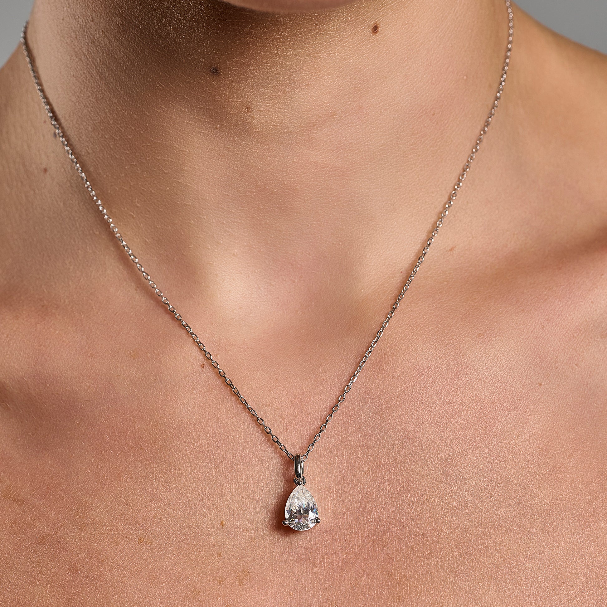 Model wearing a 925 sterling silver necklace with a 1 ct pear cut moissanite pendant in a minimalist neckline close-up.