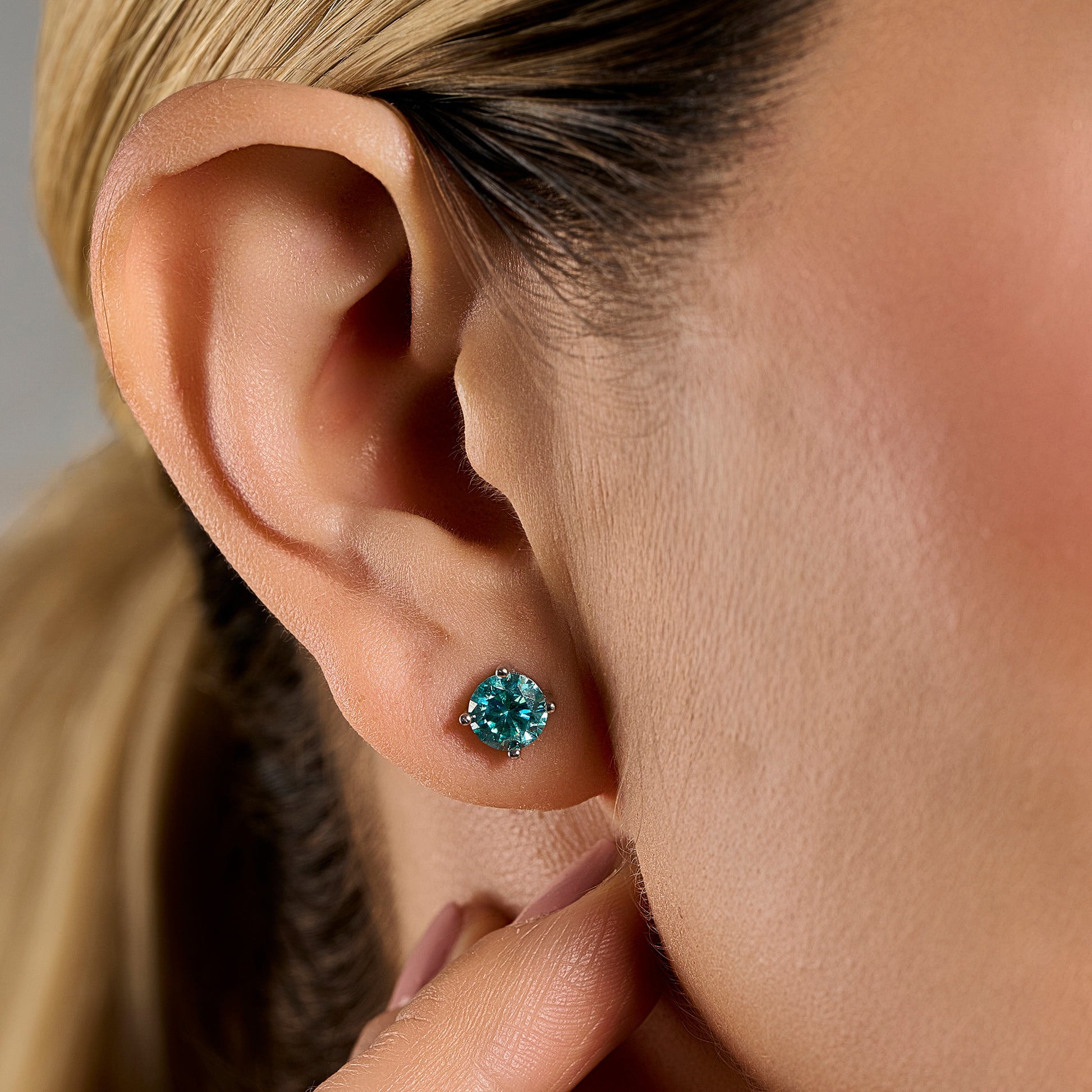Close-up lifestyle image of a woman wearing a Summer Edition round aquamarine earring featuring a 1 ct aquamarine-colored moissanite set in sterling silver.