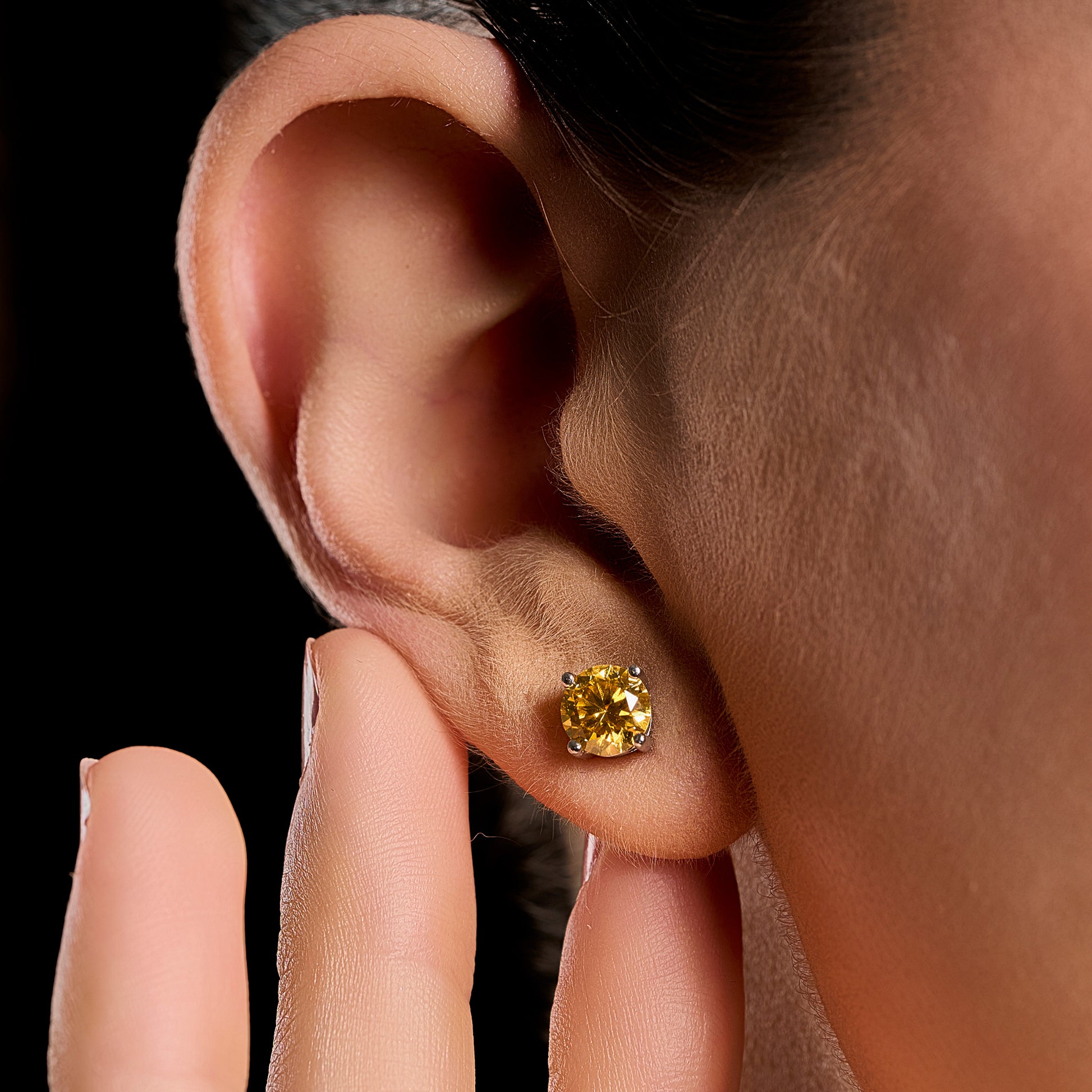 Close-up lifestyle image of a woman wearing a Summer Edition round yellow earring featuring a 1 ct brilliant cut yellow moissanite set in 925 sterling silver.