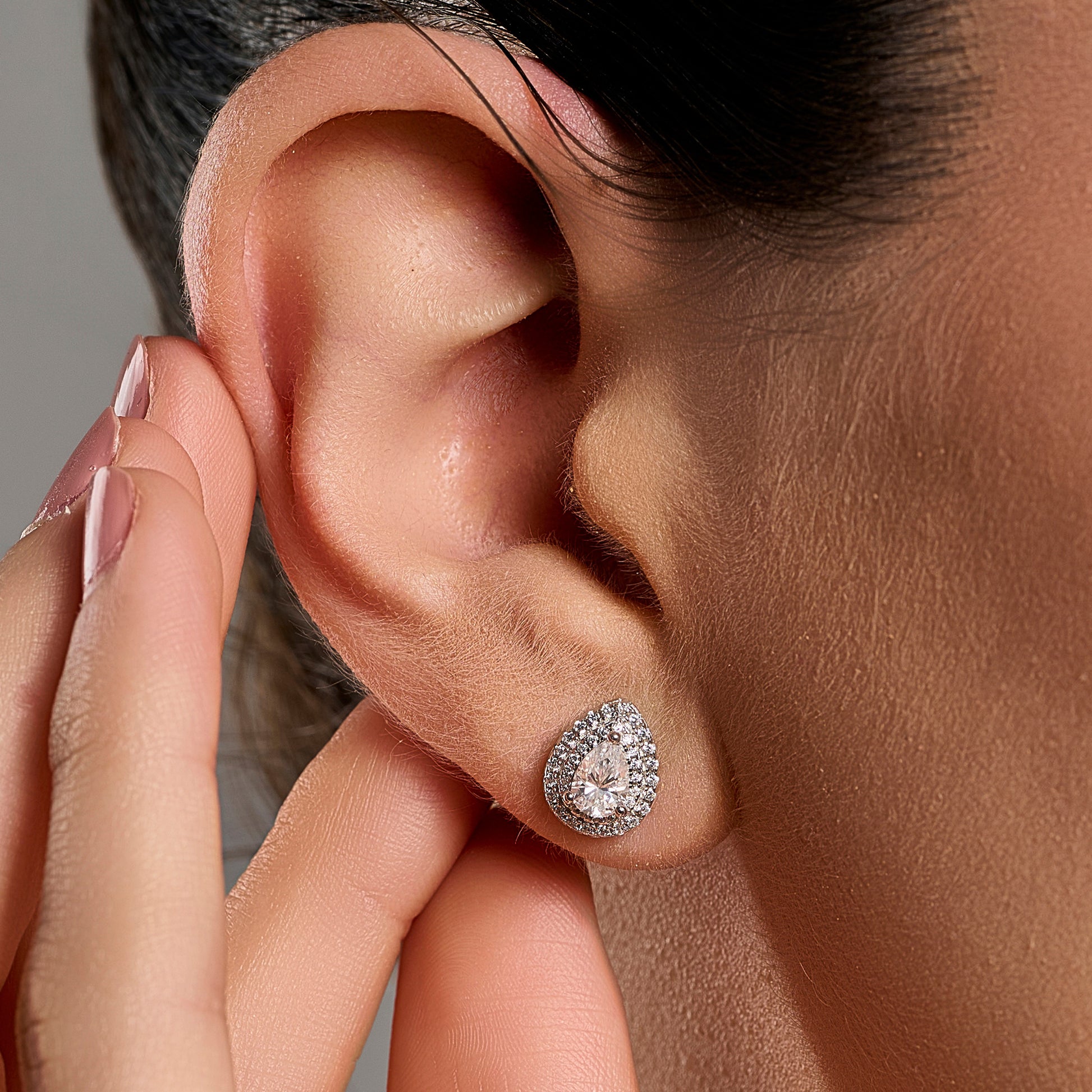 Close-up lifestyle image of a woman wearing teardrop halo earrings with 0.5 ct pear cut moissanite stones in 925 sterling silver.