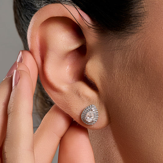 Close-up lifestyle image of a woman wearing teardrop halo earrings with 0.5 ct pear cut moissanite stones in 925 sterling silver.